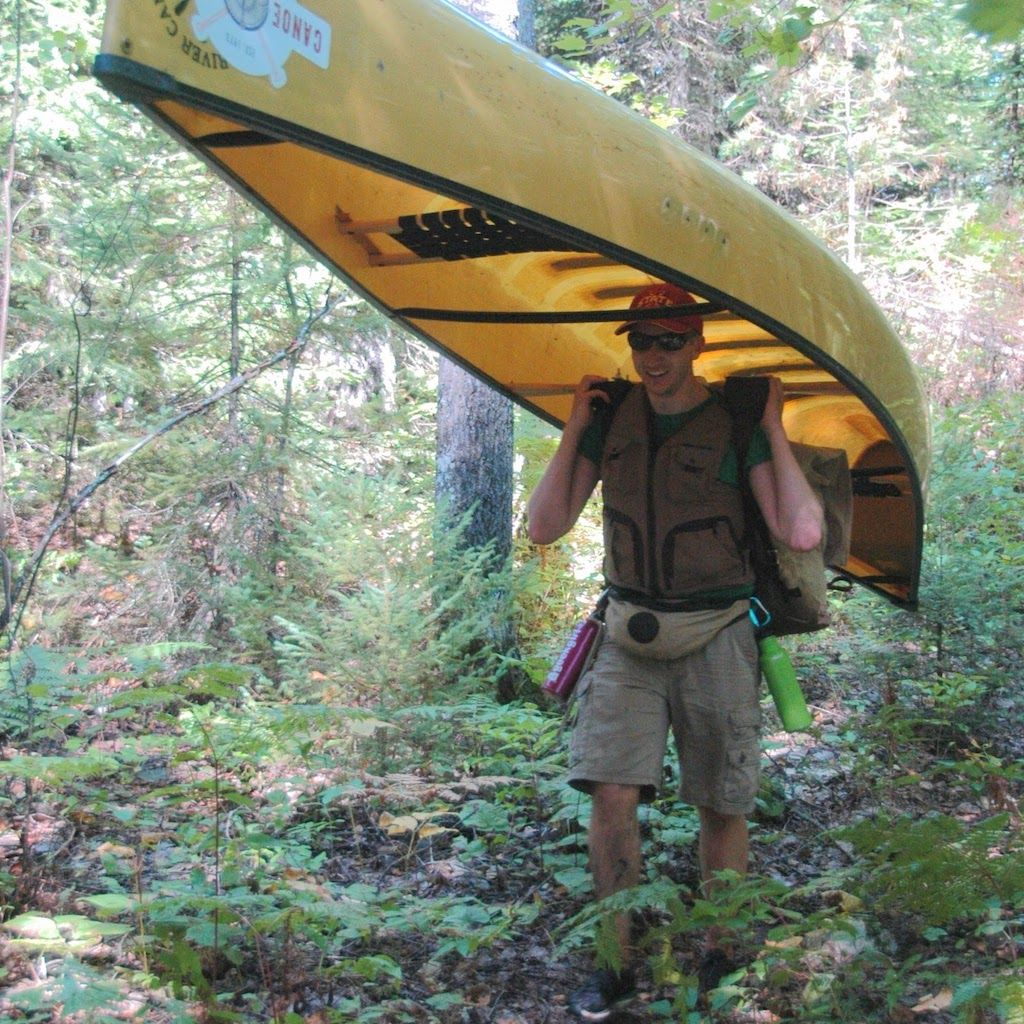 Alex carrying a canoe and Duluth pack through a forested portage area